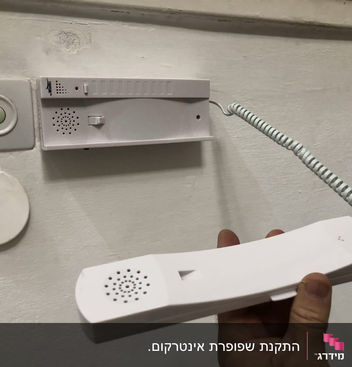 אינטרקום לבן עם שפופרת מחוברת לקיר